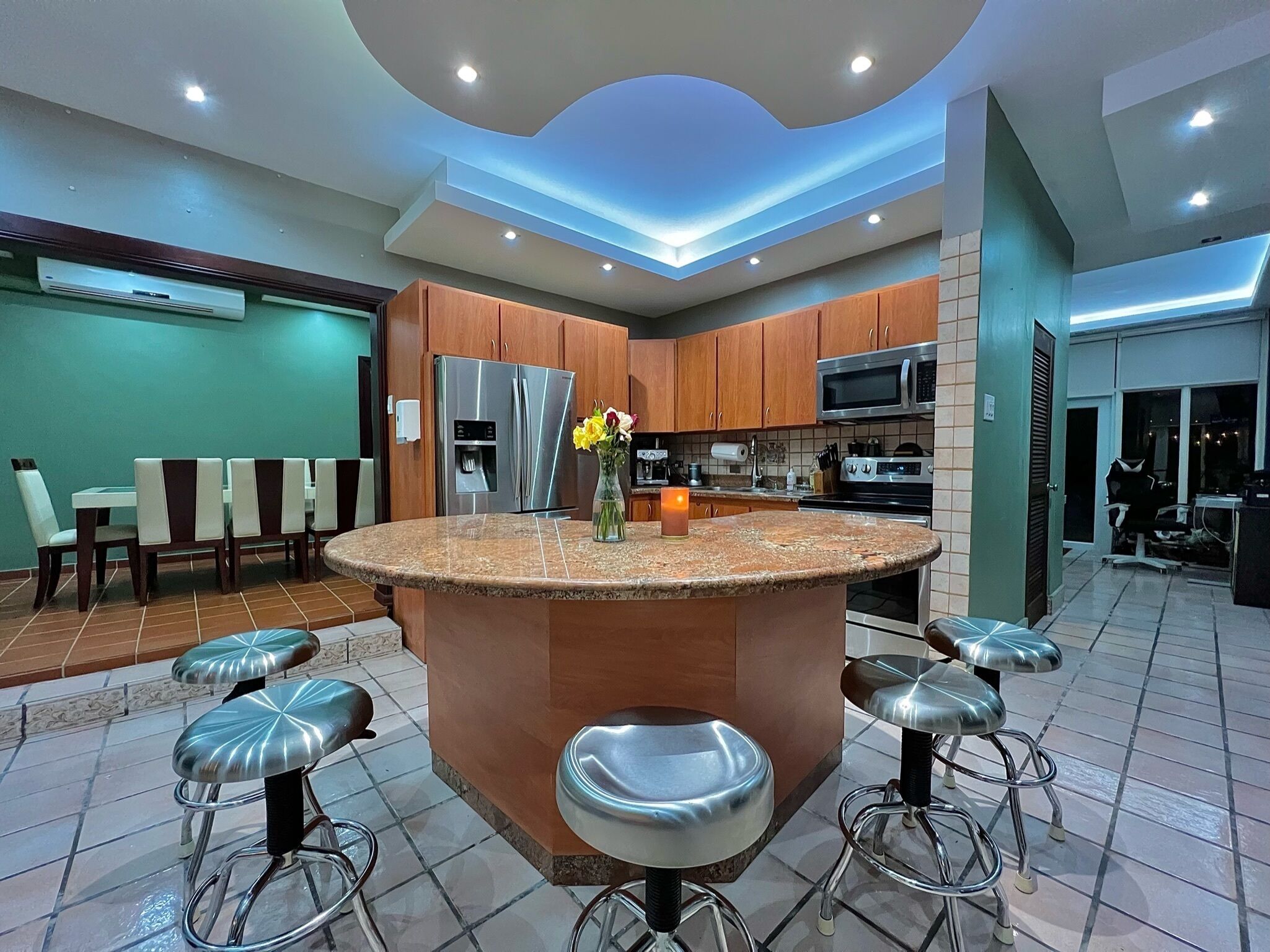 A modern kitchen with a central island, bar stools, and a dining area with chairs.