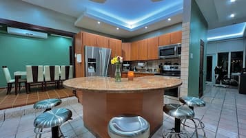 A modern kitchen with a central island, bar stools, and a dining area with chairs.