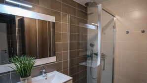 Et moderne badeværelse med et glasafskærmet brusebad, et stort spejl og en hvid vask.