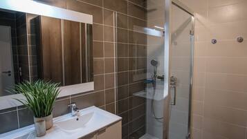A modern bathroom with a glass-enclosed shower, a large mirror, and a white sink.