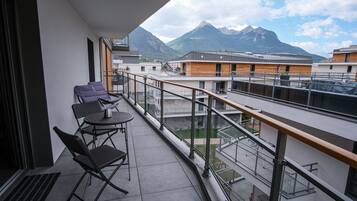 A balcony with two chairs and a small table, overlooking a mountain and other buildings.