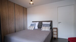 Et soveværelse med seng, garderobeskab, natbord og en dør.
