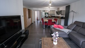 En moderne stue med et fladskærms-tv, en sofa, et sofabord med en plante og et spiseområde med røde stole.