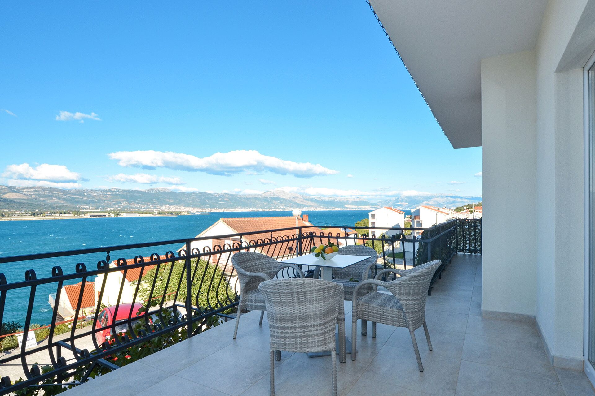 Ein Balkon mit Korbmöbeln, einem Tisch und Blick auf das Meer und die Berge.