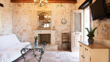 A cozy room with a stone wall, a fireplace, a white sofa, a dining table, and a TV mounted on the wall.