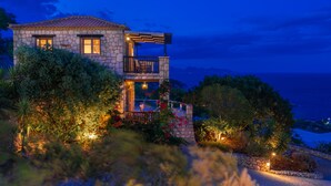 A stone house with a balcony, surrounded by lush greenery and a view of the sea. - Strofilia Authentic Villas (Zakynthos)