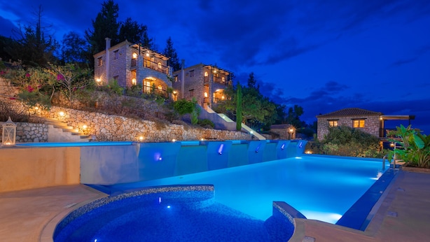 A large swimming pool with a stone wall and steps leading up to a stone building with multiple balconies. - Strofilia Authentic Villas (Zakynthos)
