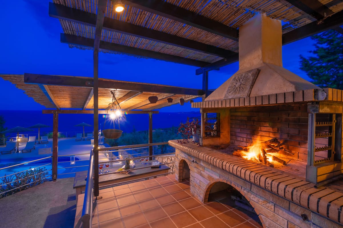An outdoor patio with a brick fireplace, lounge chairs, and a pool.