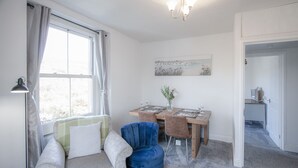 Una habitación con un sofá, una silla azul, una mesa de comedor con sillas, una araña y un cuadro en la pared.