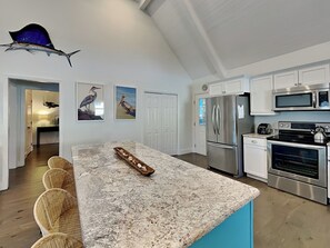A modern kitchen with white cabinetry, stainless steel appliances, a granite countertop, and a large island with seating.