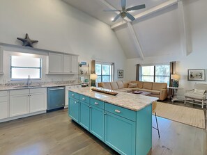 A spacious kitchen with a large island, a dining area with a sofa, and a ceiling fan. - Live Oaks Cottage | Breezy Porches, Fire Pit, Ping Pong Table (Tybee Island)