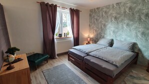 A bedroom with a bed, a small table with a globe, a bench, a window with curtains, a radiator, and a patterned wall. - Rural, by the North Sea, family-friendly, sauna and whirlpool! (Schiffdorf)