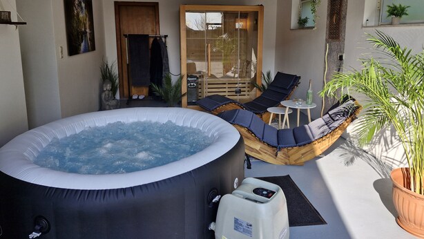 A hot tub in a sunlit outdoor area with lounge chairs and a small table. - Rural, by the North Sea, family-friendly, sauna and whirlpool! (Schiffdorf)