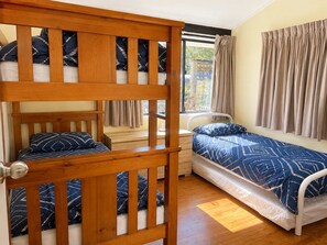 A room with a bunk bed, a single bed, and a window with curtains.