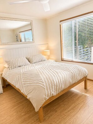 A bedroom with a large bed, two bedside lamps, a window with blinds, and a mirror on the wall.