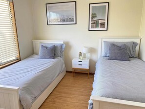 A twin bedroom with two beds, a nightstand, and two framed pictures on the wall.