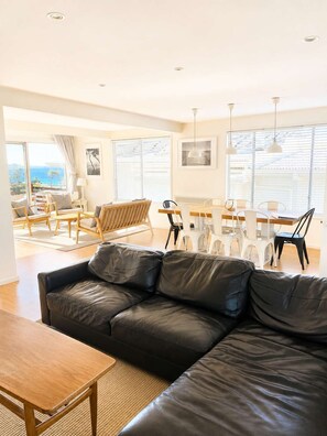 A modern living room with a leather sofa, wooden coffee table, and dining area with white chairs.