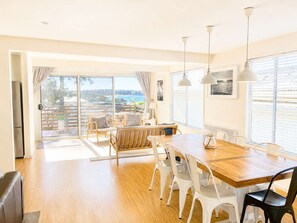 A spacious dining area with a wooden table and chairs, large windows with a view, and pendant lighting.