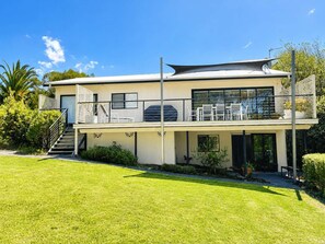 A modern two-story house with a flat roof, large windows, and a balcony with outdoor furniture. - Sea Breeze On Carroll (Mollymook)
