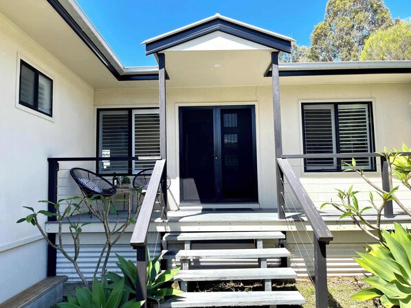A modern house with a covered porch, a staircase, and a sliding glass door. - Sea Breeze On Carroll (Mollymook)