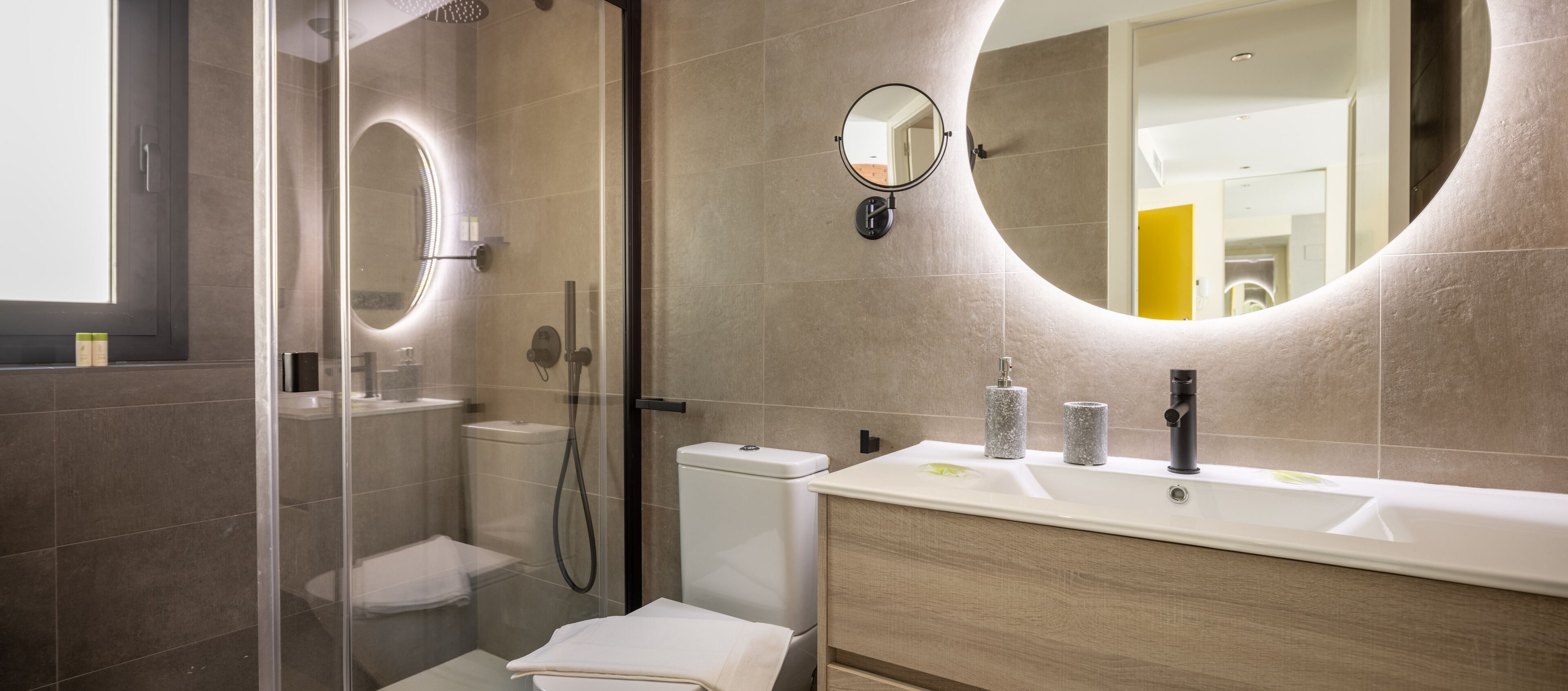 A modern bathroom with a glass-enclosed shower, a toilet, a sink with a marble basin, and a large mirror.