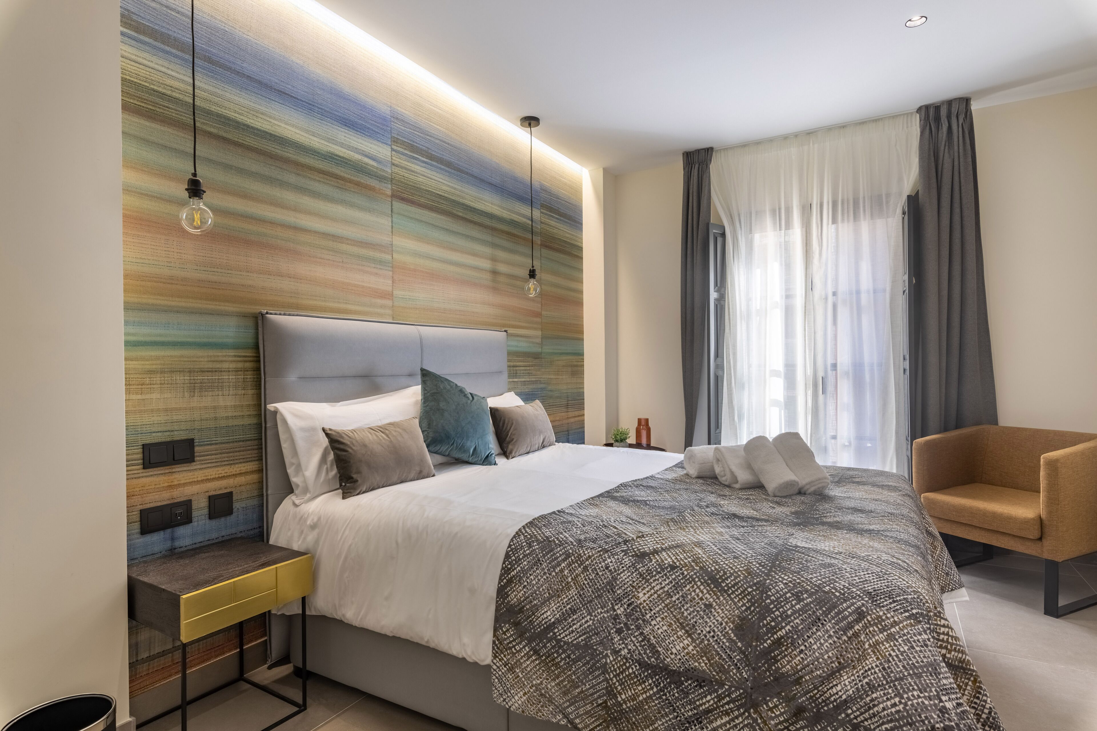 A modern bedroom with a large bed, bedside tables, a chair, and a wall with a textured design.
