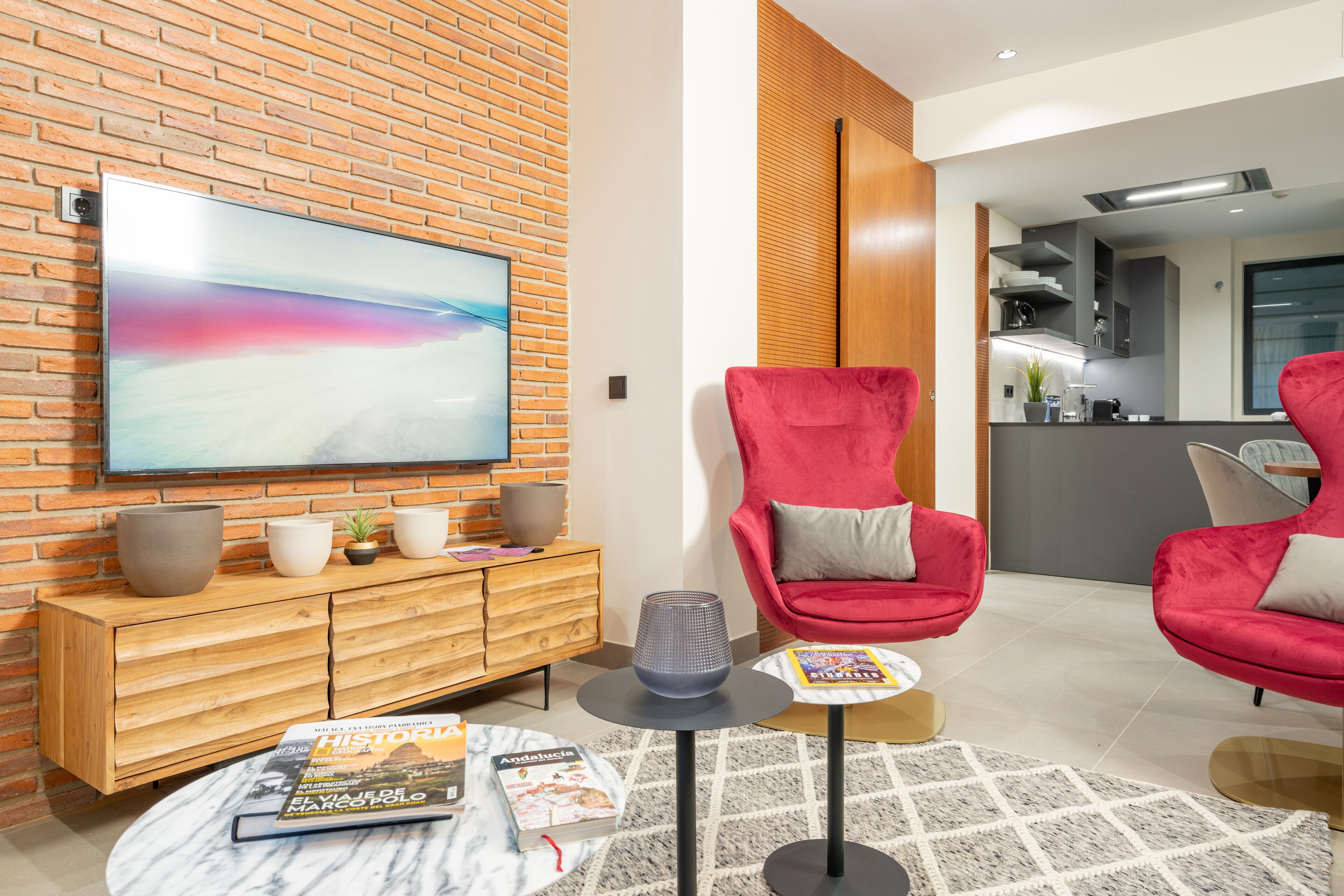 Een moderne woonkamer met een grote flatscreen televisie, rode stoelen, een houten kast en een tijdschrift op een salontafel.