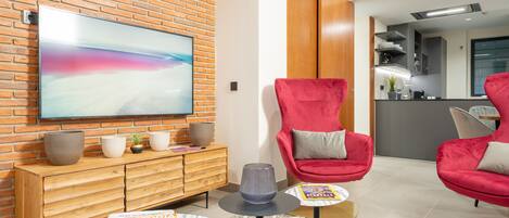 Een moderne woonkamer met een grote flatscreen televisie, rode stoelen, een houten kast en een tijdschrift op een salontafel.