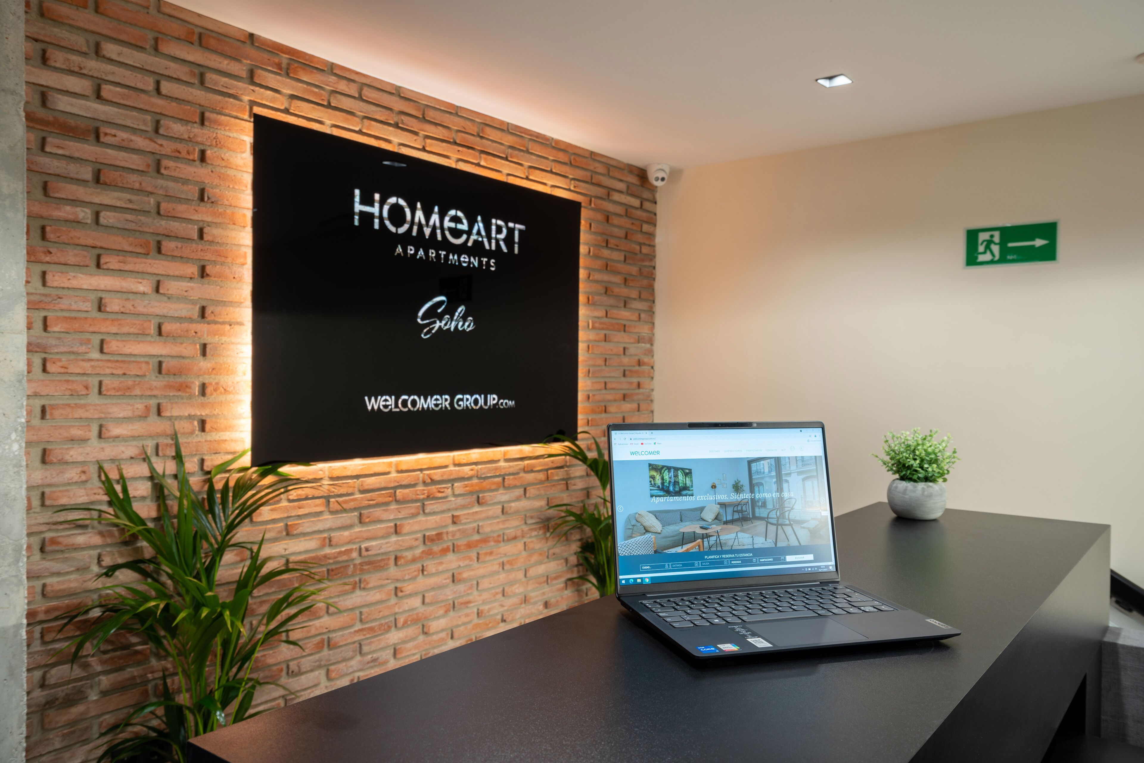 A reception desk with a laptop, a sign for HOMEARTH APARTMENTS, and a small potted plant.