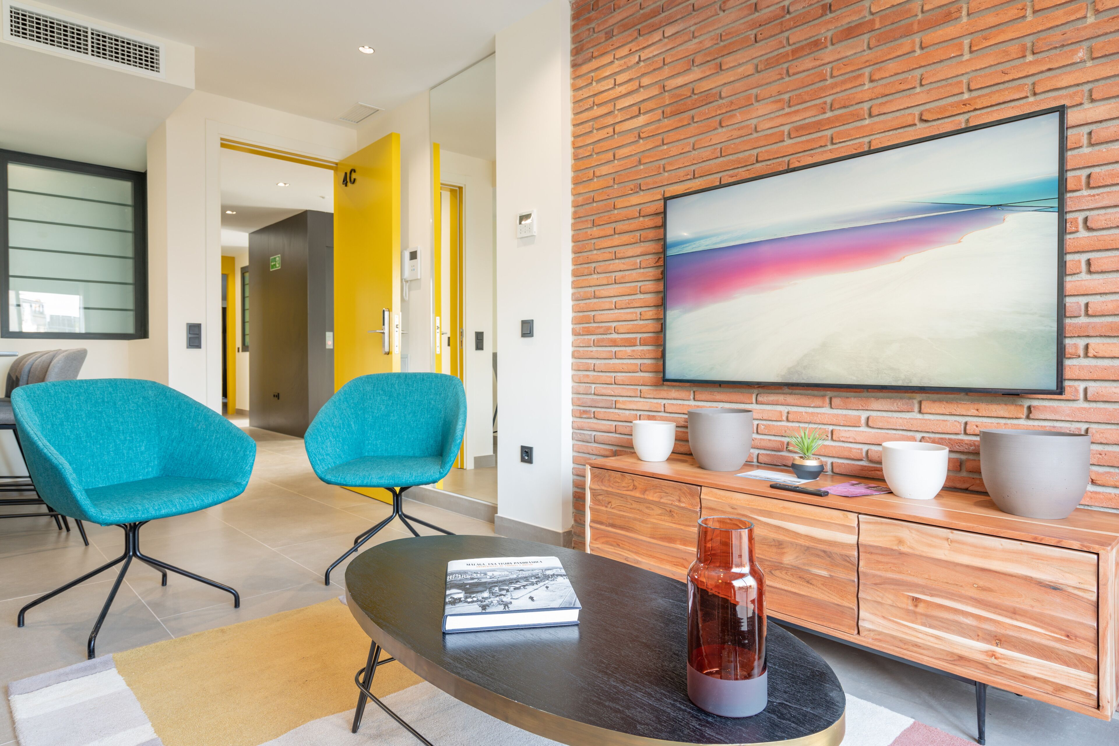 Een moderne woonkamer met twee teal-kleurige fauteuils, een salontafel, een boek, een vaas en een groot schilderij op een bakstenen muur.