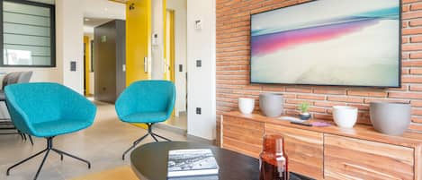 Een moderne woonkamer met twee teal-kleurige fauteuils, een salontafel, een boek, een vaas en een groot schilderij op een bakstenen muur.