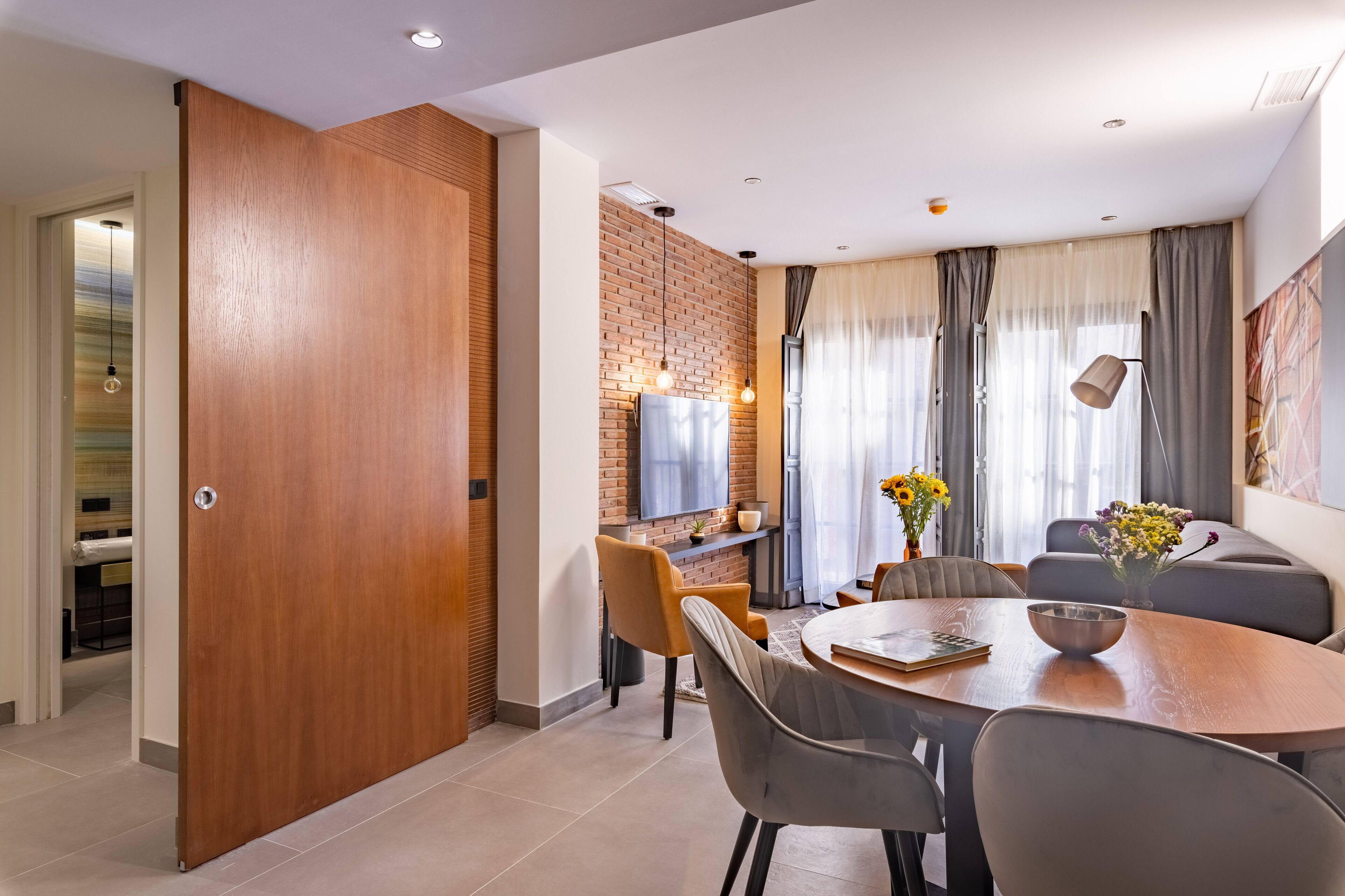 A modern dining area with a wooden door, a brick accent wall, a TV, and a dining table with chairs.