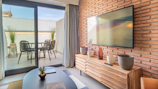 Ett modernt vardagsrum med en stor TV, en träkonsol och en skjutdörr i glas som leder ut till ett utomhusområde med stolar och växter.