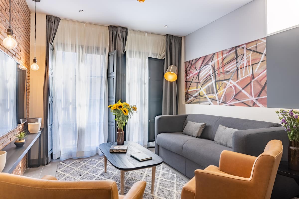 A modern living room with a grey sofa, orange armchairs, a wooden coffee table, and a vase of sunflowers.