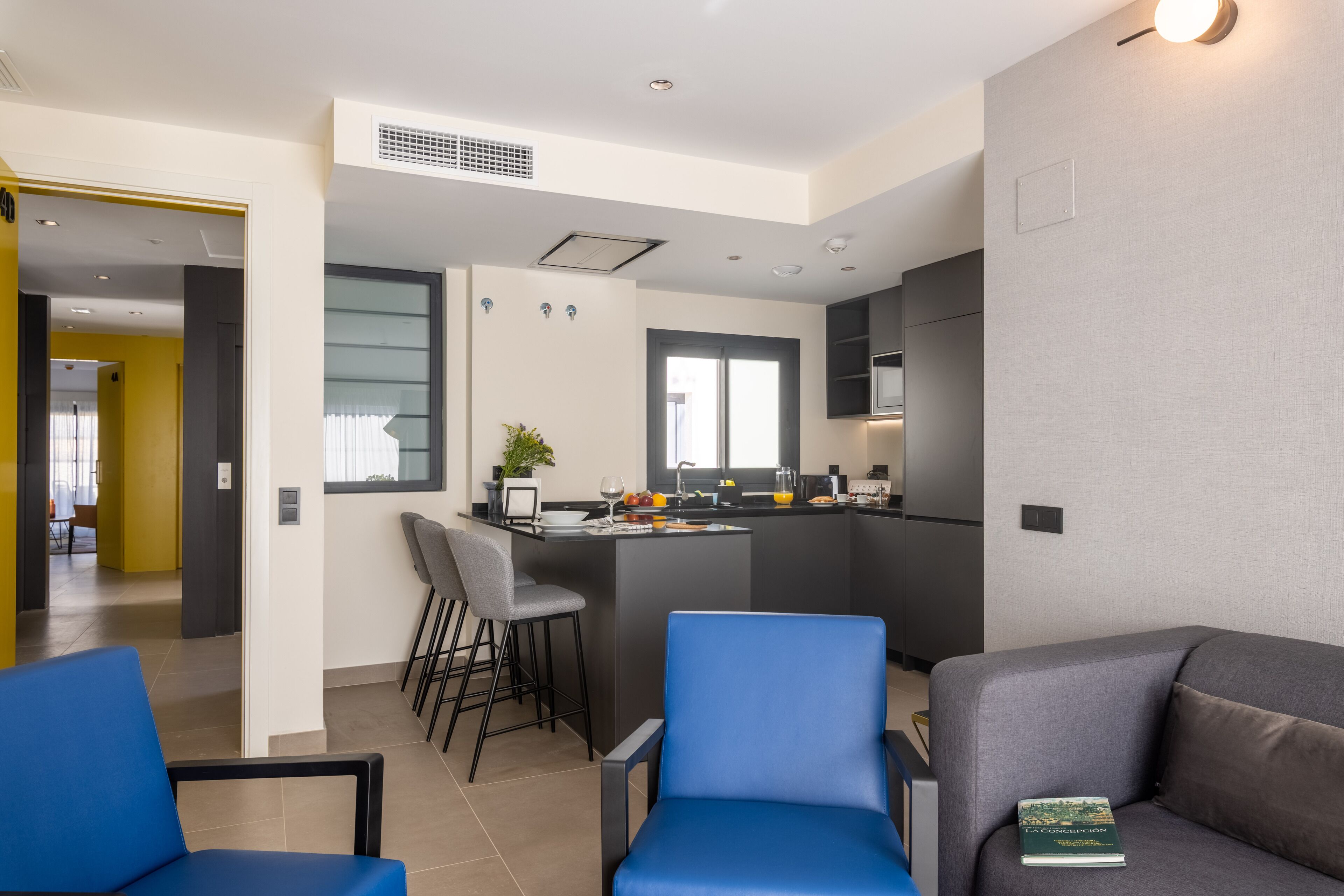 A modern kitchen with a central island, bar stools, and a dining area with a blue chair.