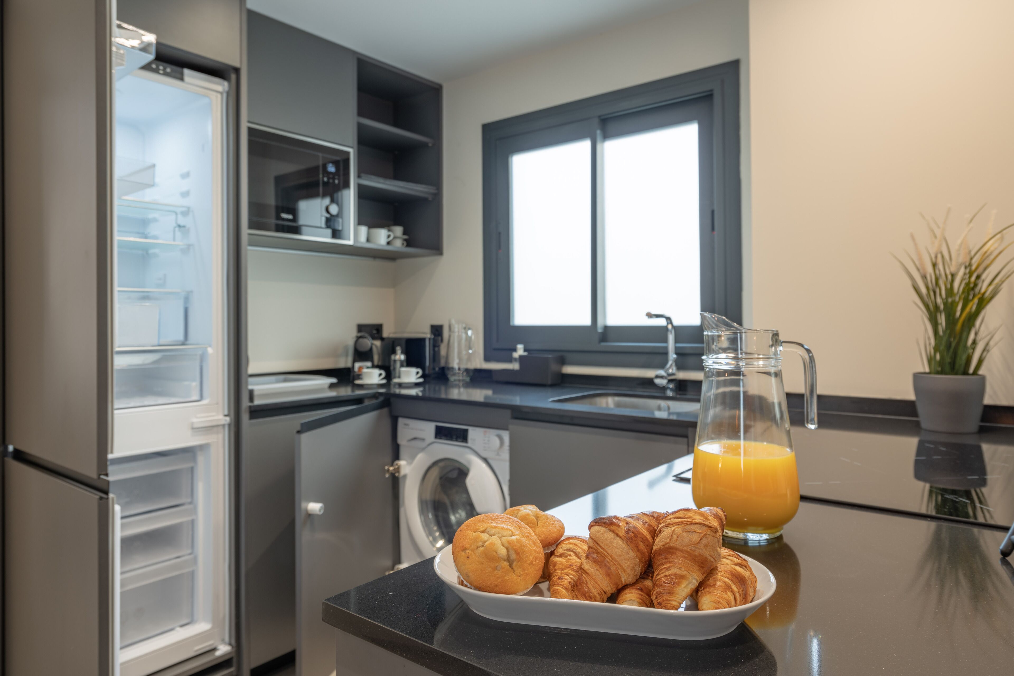 Una cocina moderna con refrigerador incorporado, lavadora, pileta y ventana.