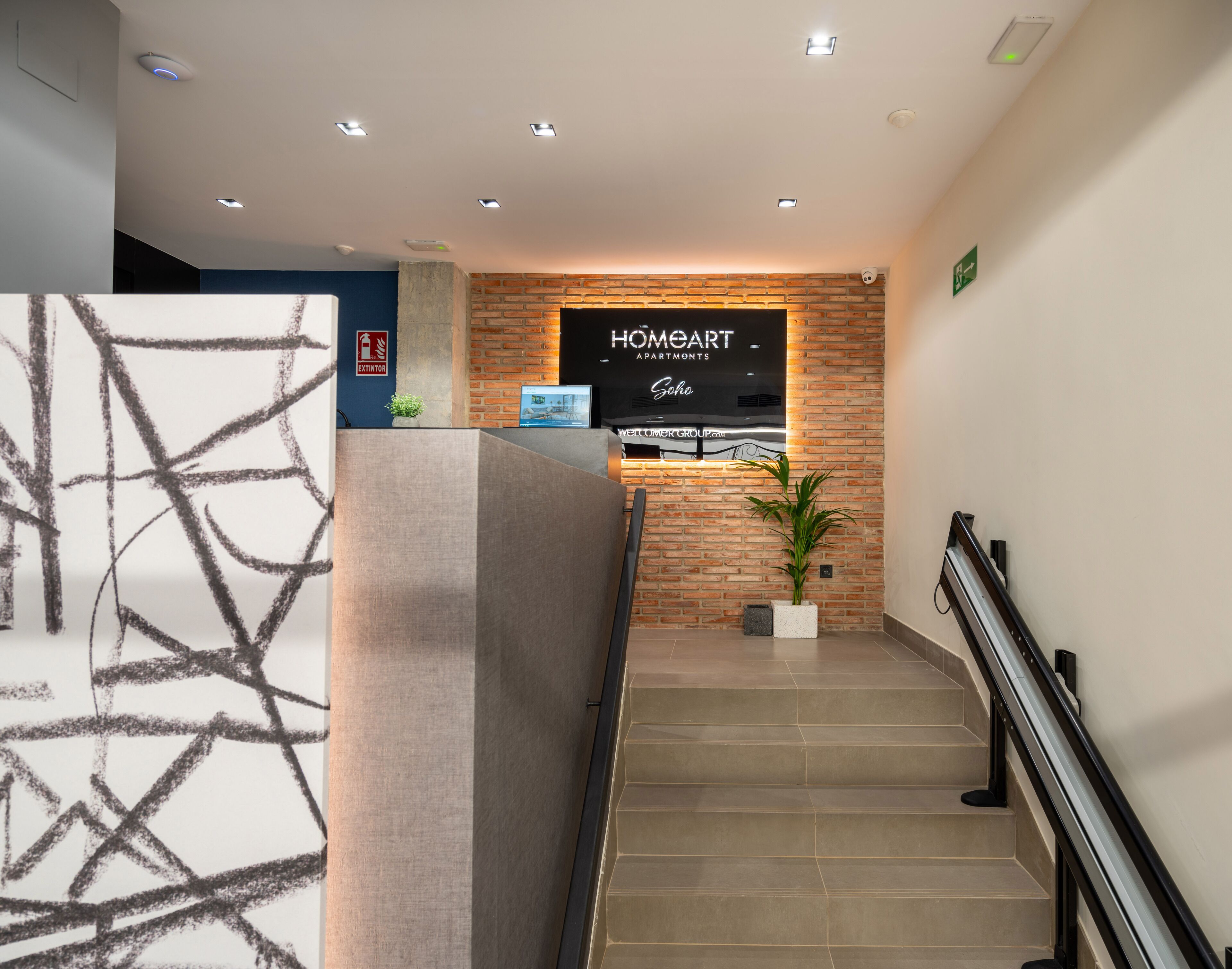 A reception area with a brick wall, a digital display, and a staircase.