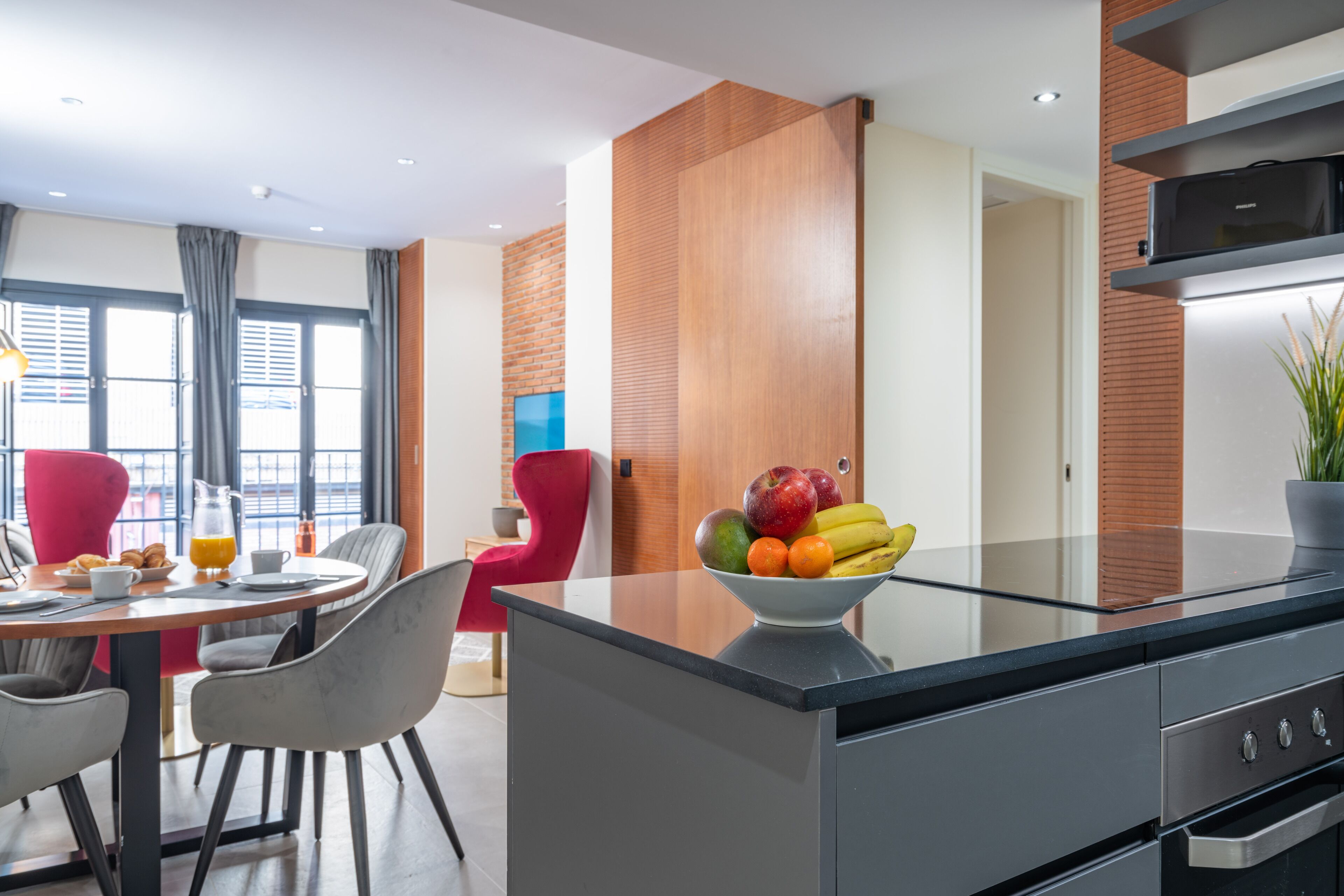 A modern kitchen with a glass island, a dining area with a red chair, and a breakfast setting.