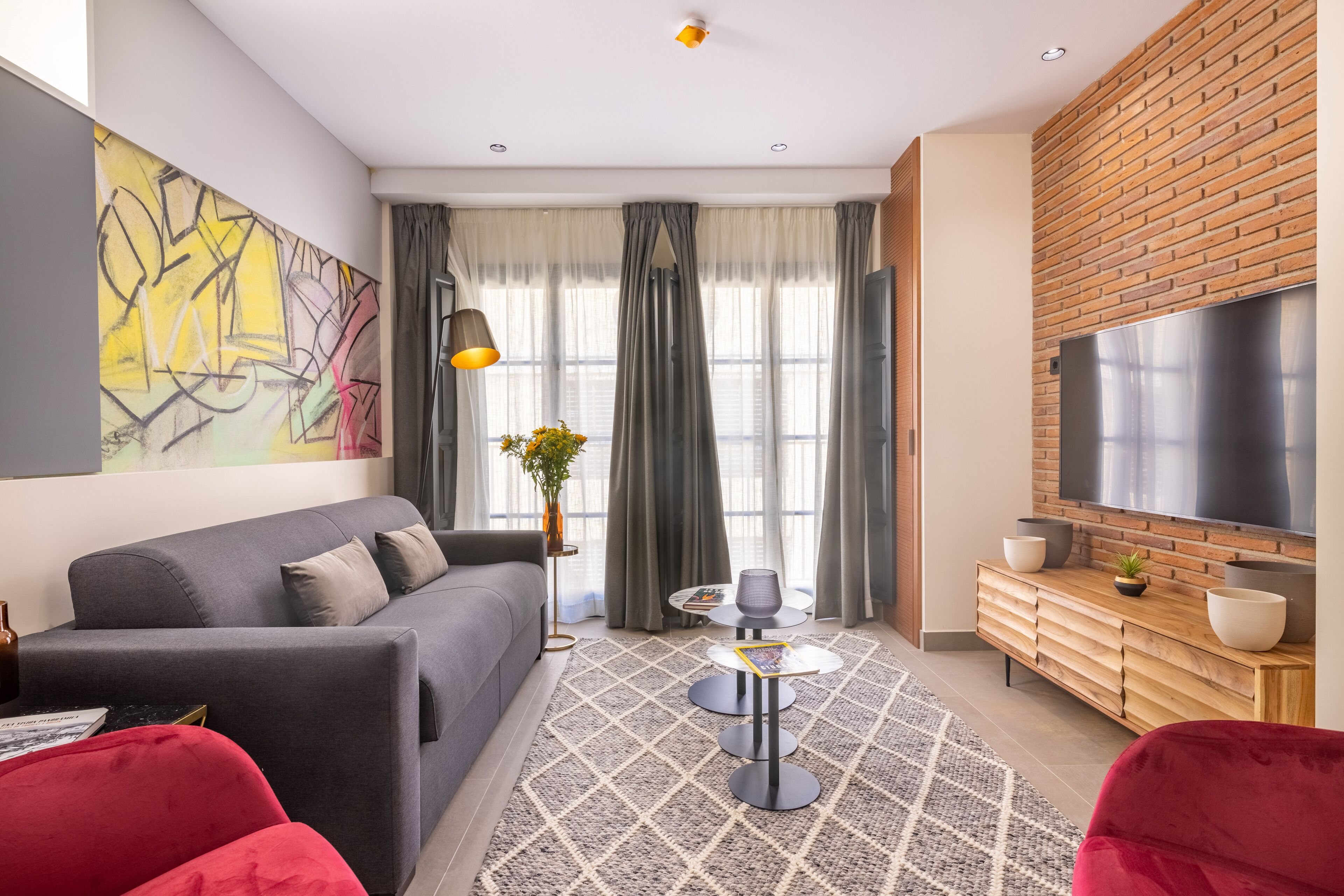 Ein modernes Wohnzimmer mit grauem Sofa, rotem Sessel und einem an einer Ziegelwand montierten Fernseher.