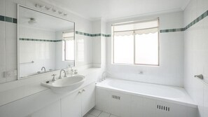 A bathroom with a sink, mirror, window, and bathtub.