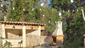 Un'area patio esterna con un tavolo in vetro, un barbecue e luci a stringa.