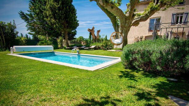 Una piscina rettangolare con bordo bianco, circondata da prato curato e alberi.
