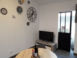 A modern room with a flat-screen TV, a wooden dining table, and wall-mounted clocks labeled 'SYDNEY' and 'JOHANNESBURG'.