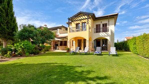 A two-story house with a balcony, a well-maintained lawn, and a garden with various plants and trees. - Apartment A02 - Roudias (Kouklia)