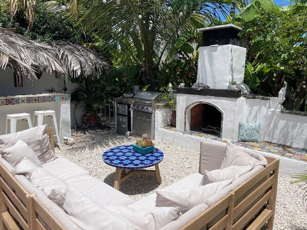 An outdoor patio with a round table, cushioned seating, a grill, and a decorative oven. - Malecon Beach House with beautiful backyard. Steps from the Caribbean ocean. (PATILLAS)