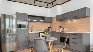 A modern kitchen with grey cabinetry, a stainless steel refrigerator, a microwave, and a dining area with two grey chairs and a small table. - 1 Bedroom on Century City Urban Square (Cape Town)