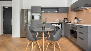 A modern kitchen with a dining table, chairs, a refrigerator, microwave, oven, and a coffee maker. - 1 Bedroom on Century City Urban Square (Cape Town)
