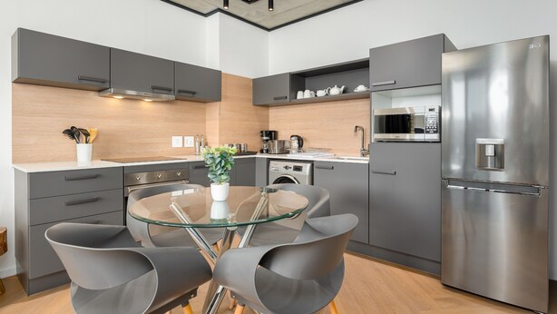 Una cocina moderna con armarios grises, un refrigerador de acero inoxidable, una mesa de comedor de superficie de vidrio y un microondas.