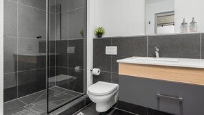 Un baño moderno con cabina de ducha de vidrio, inodoro y tocador con espejo.