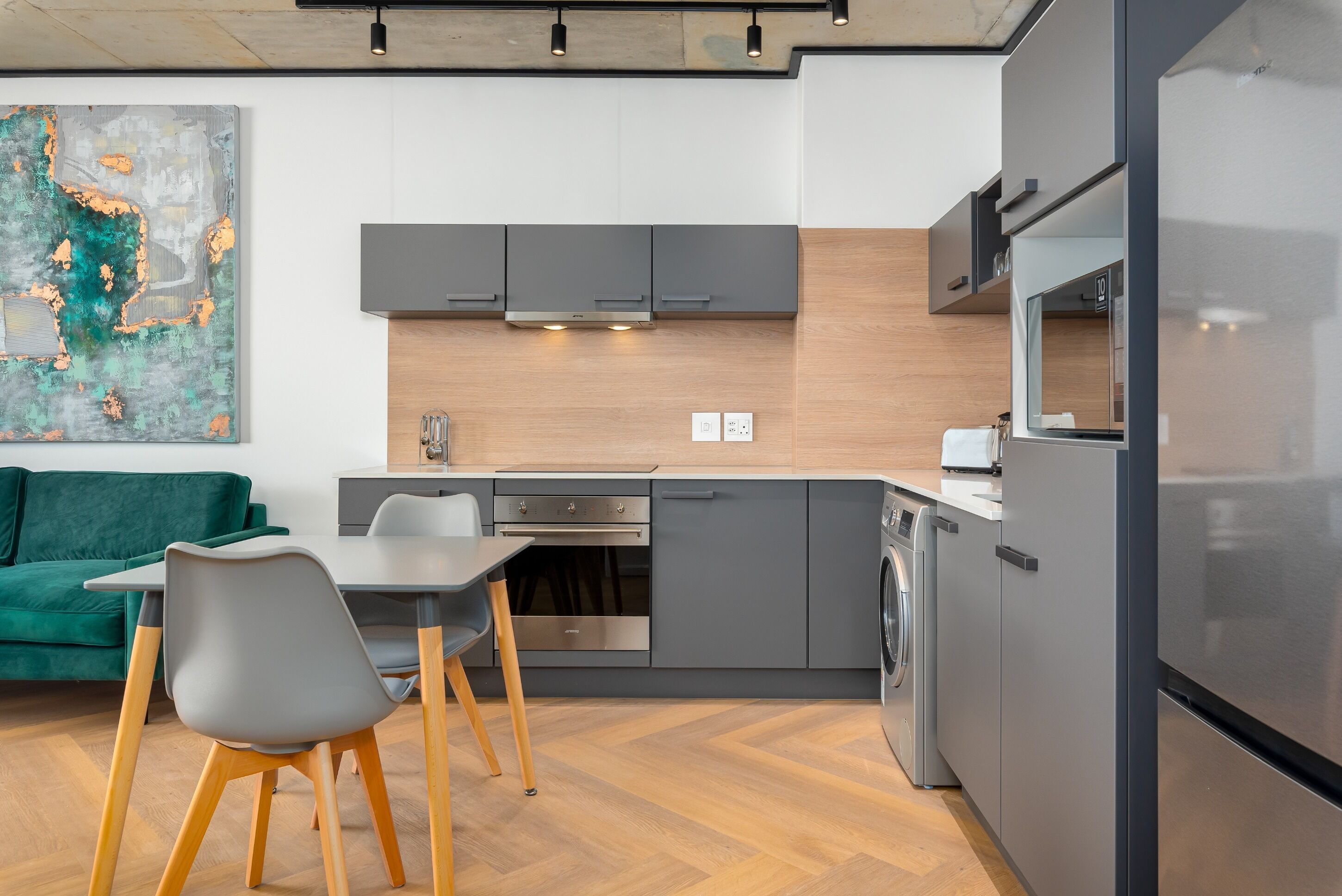 A modern kitchen with grey cabinets, a stainless steel refrigerator, and a washing machine.